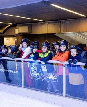 Kids all laced up with skates and have helmets on as they interact with Minister Chow 