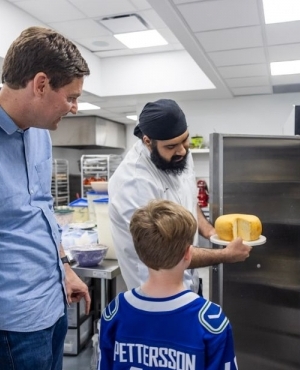 Baker Jujhar Mann proudly shows his cake creation to Premier David Eby's son