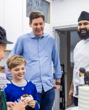 Baker, Premier David Eby, his son look at the cake with intrigue 